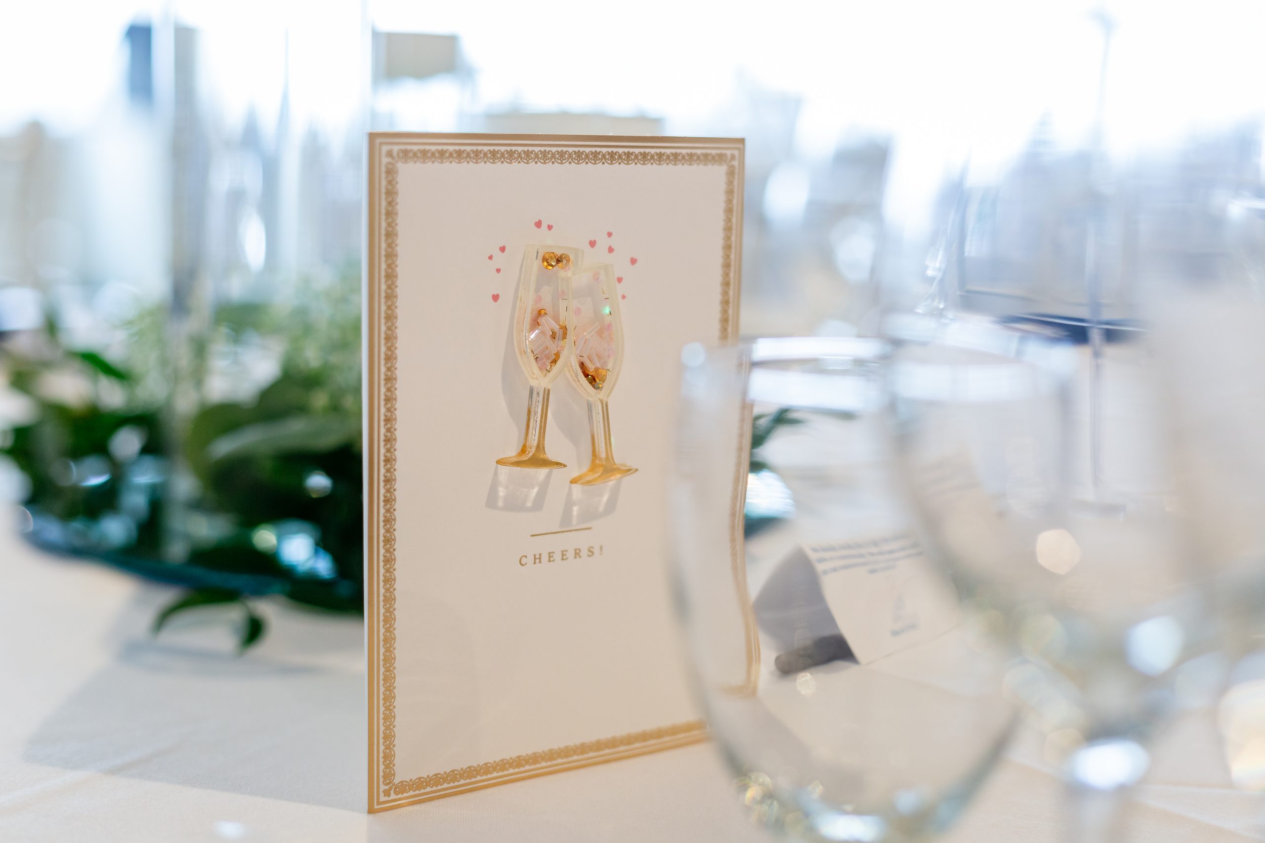 Champagne-themed “Cheers” card displayed beside glassware at a bridal shower.