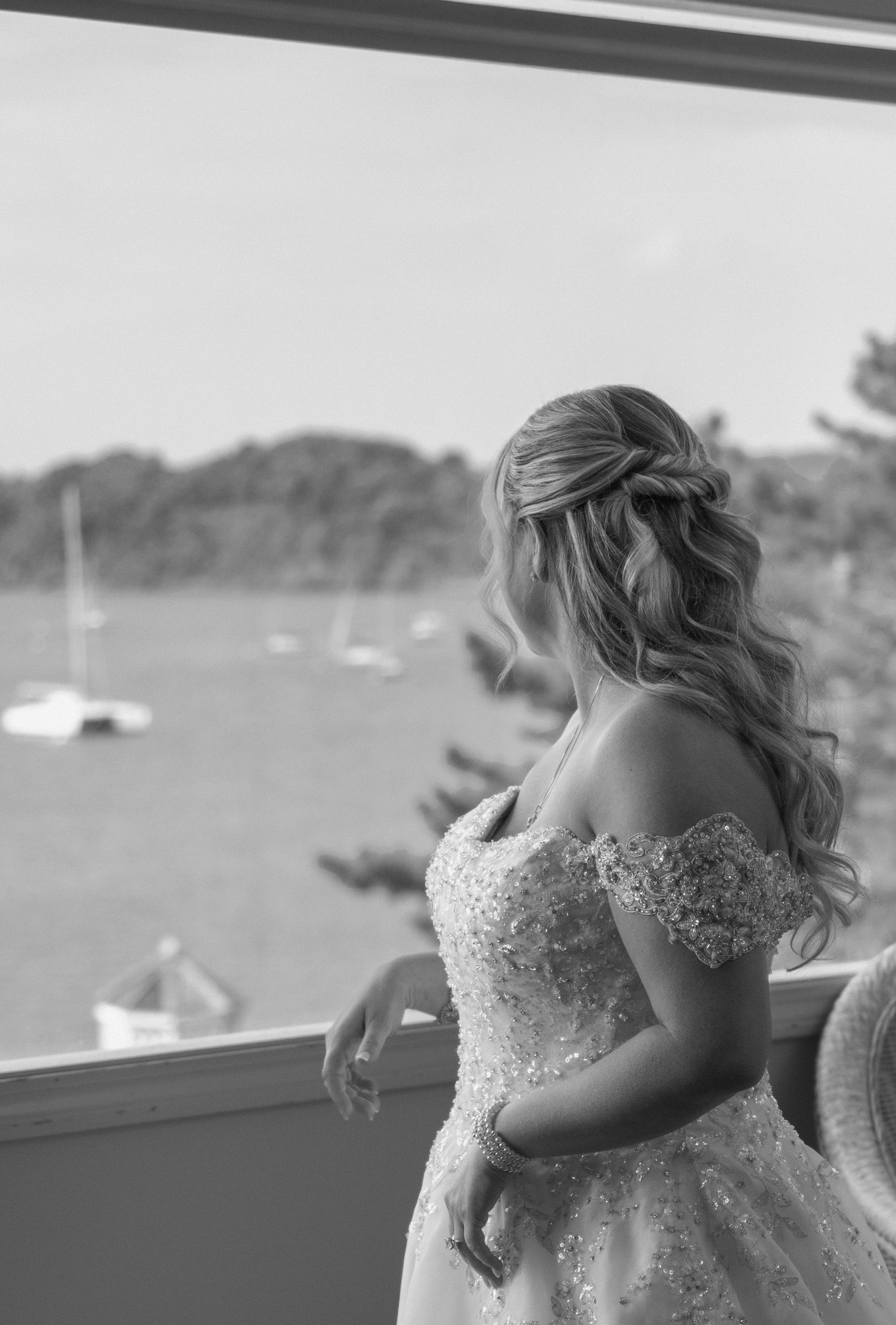Bride in a wedding gown looking out over the water and boats from a window at Amarante's Sea Cliff in New Haven, Connecticut