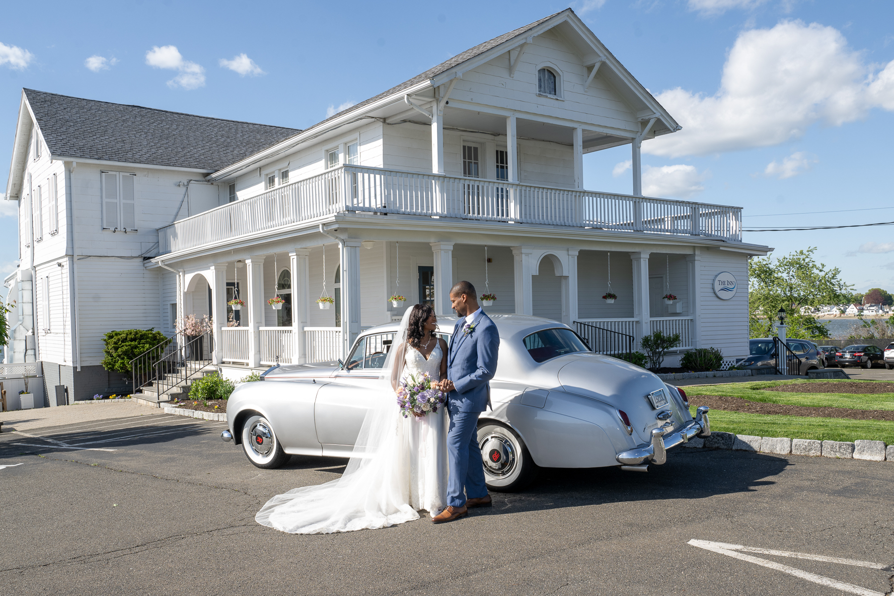 Newlyweds standing beside a vintage car outside The Inn at Amarante’s Sea Cliff.